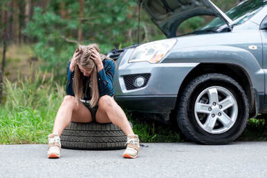 A frustrated lady sitting a tire because of a flat tire.